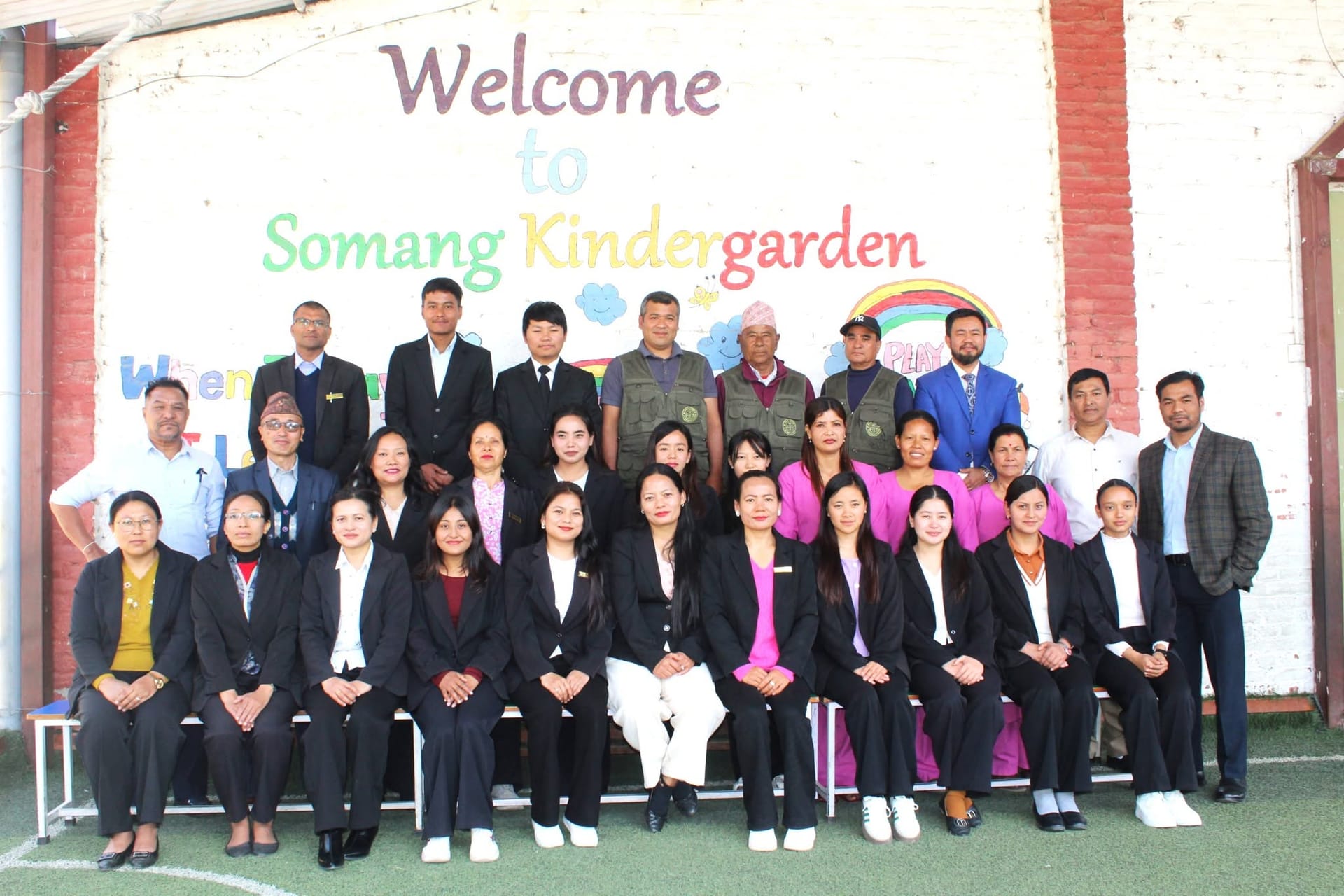 The Somang Academy teachers and staff team in front of the welcome wall